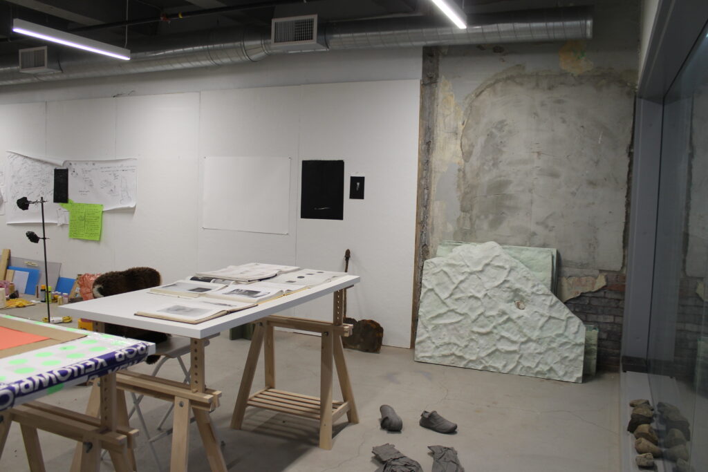Studio with white and cement walls, white drafting table on the left, large textured sculpture on the right